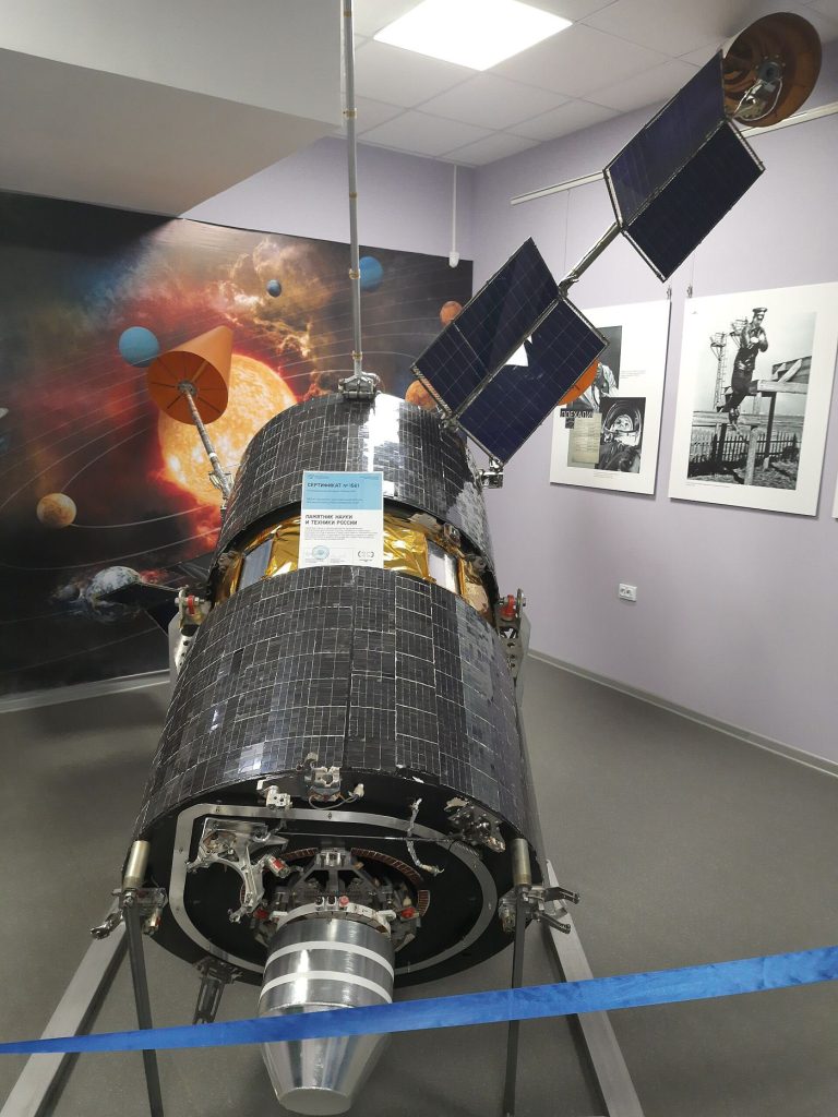 A communications satellite orbits above Earth with solar panels extended against the planet below.